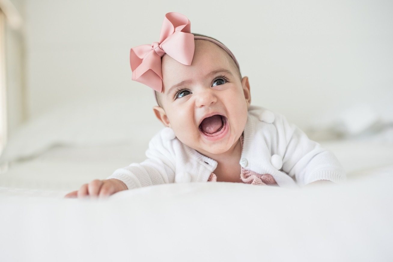 Bebê de laço rosa sorrindo na luz suave da janela